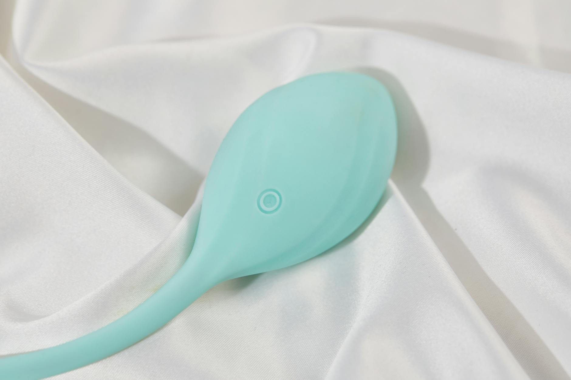 A stylish teal vibrator on smooth white silk fabric, representing modern pleasure tools