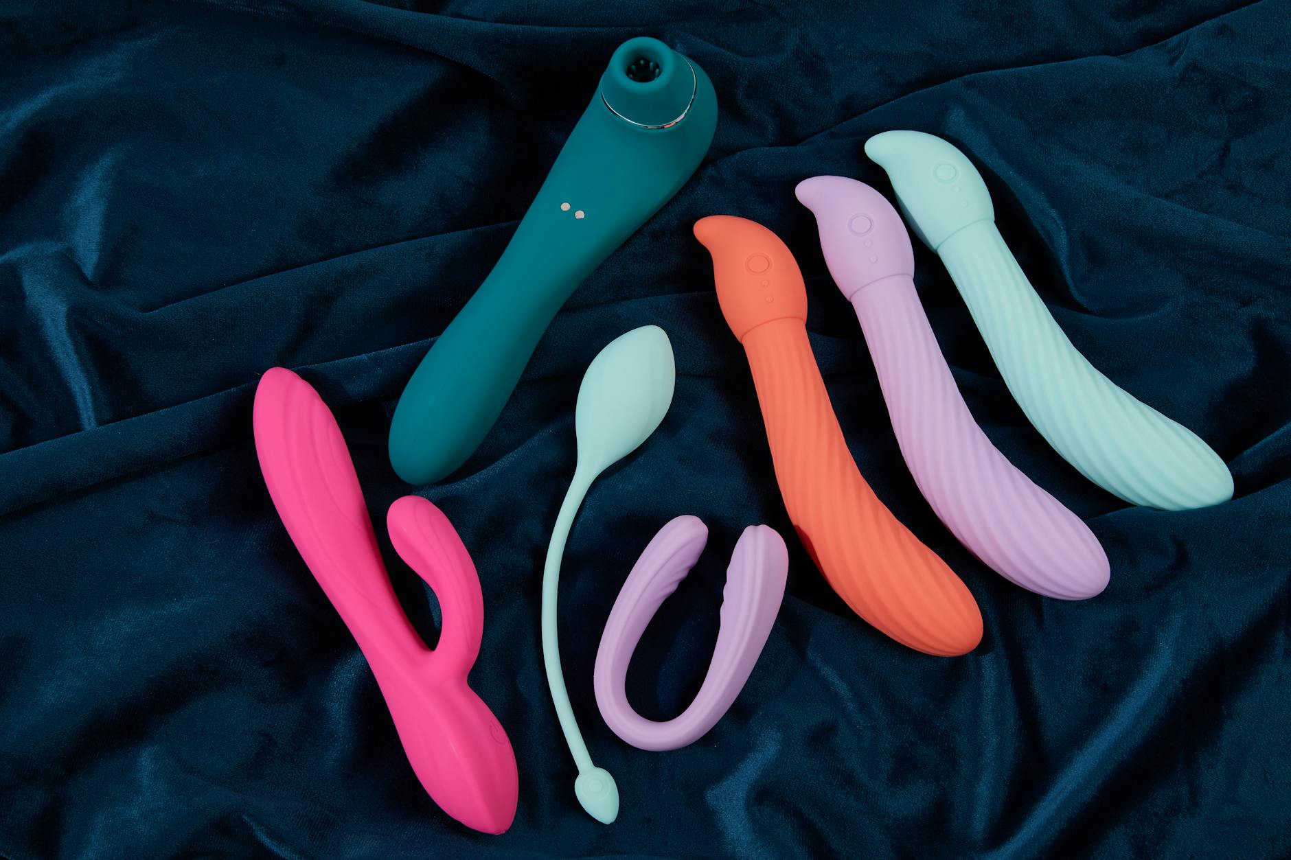 Woman holding blue and pink silicone vibrators in a contemplative manner