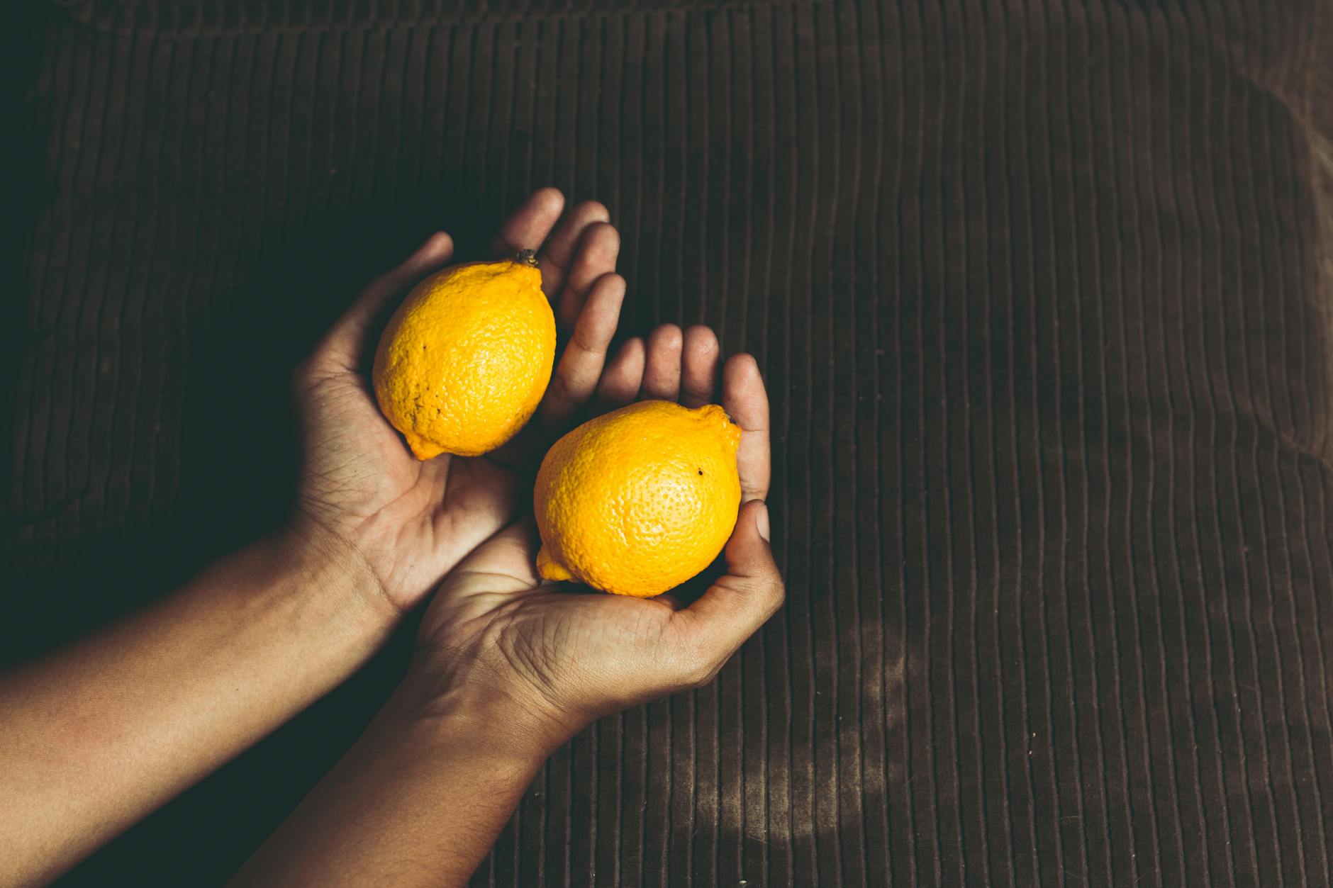 Close-up of two fresh lemons held in cupped hands on a brown surface, symbolizing freshness and new beginnings.