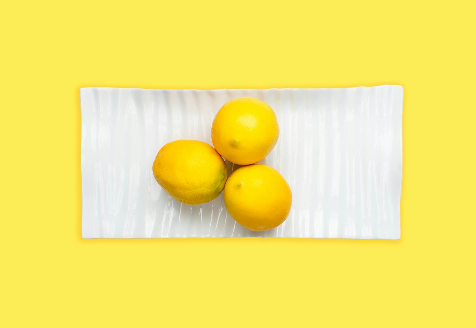 Fresh lemons arranged on a white plate with vibrant yellow background, symbolizing renewal and sensory awakening
